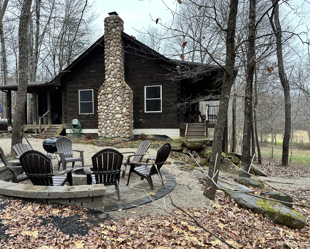 Fire pit patio and Adirondack chairs beside the log cabin and stone chimney