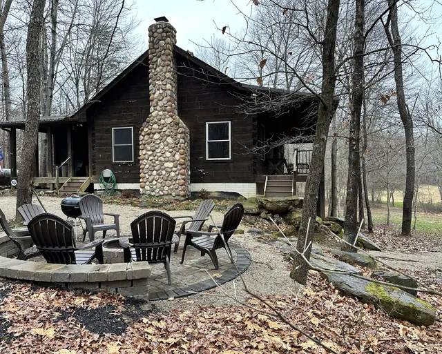 Fire pit patio and Adirondack chairs beside the log cabin and stone chimney