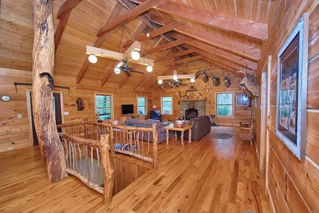 Great room with a vaulted log ceiling, handmade log railing and stone fireplace