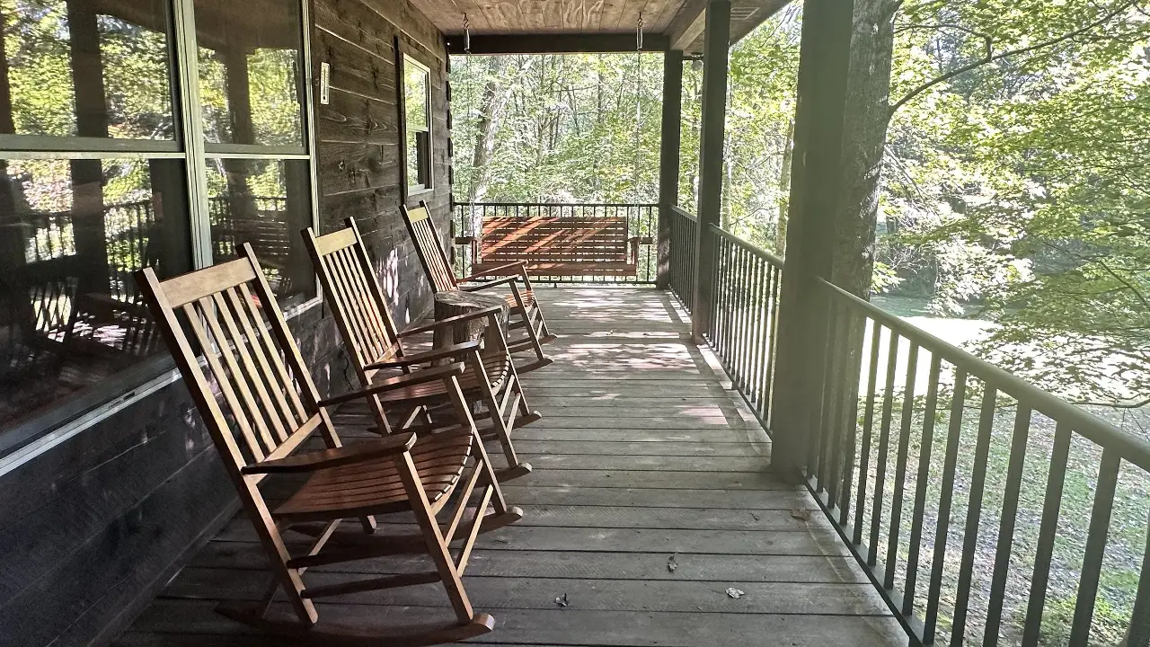 Rocking chairs and a porch swing on the covered porch of Serenity Lodge, a Hocking Hills cabin with hot tub, looking into the woods